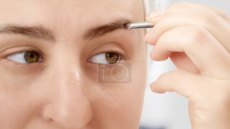 Photo for Macro shot of woman plucking eyebrows with small cosmetic tweezers at home. Concept of beautiful female, makeup at home, skin care and domestic beauty industry - Royalty Free Image