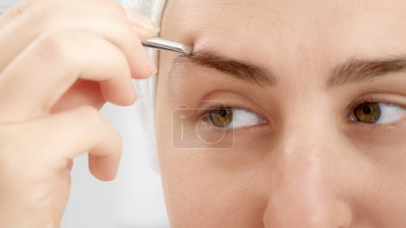 Photo for Closeup portrait of smiling young woman forming eyebrows with tweezers after having bath. Concept of beautiful female, makeup at home, skin care and domestic beauty industry - Royalty Free Image