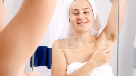 Téléchargez les photos : Femme souriante regardant et touchant ses aisselles poilues après le lavage sous la douche. Concept de belle femme, beauté naturelle, féminité et poils du corps - en image libre de droit