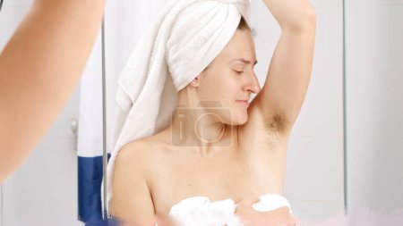 Téléchargez les photos : Jeune femme sentant ses aisselles puantes avec des cheveux qui poussent à la salle de bain. Concept d'hygiène, beauté naturelle, féminité et croissance des poils du corps - en image libre de droit
