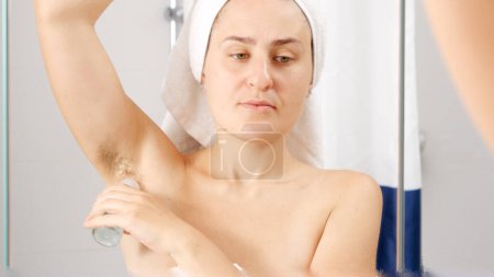 Téléchargez les photos : Jeune femme avec les cheveux aisselle application de déodorant pour éliminer la mauvaise odeur et l'odeur. Concept d'hygiène, beauté naturelle, féminité et croissance des poils du corps - en image libre de droit