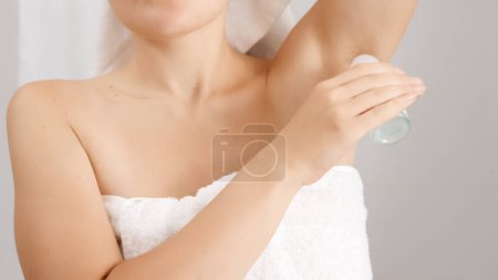 Téléchargez les photos : Gros plan de la femme couverte de serviette de bain blanche soulevant son bras et utilisant du déodorant. Concept d'hygiène, beauté naturelle, féminité et croissance des poils du corps - en image libre de droit
