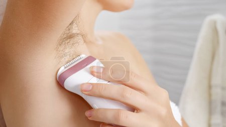 Photo for Closeup of young woman with long armpit hair making depilation with electric epilator. Concept of hygiene, natural beauty, feminity and body hair growth - Royalty Free Image