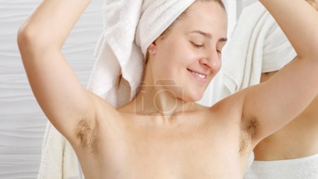 Foto de Retrato de mujer natural sonriente con el pelo de la axila creciendo posando en el baño. Concepto de higiene, belleza natural, feminidad y crecimiento del vello corporal - Imagen libre de derechos