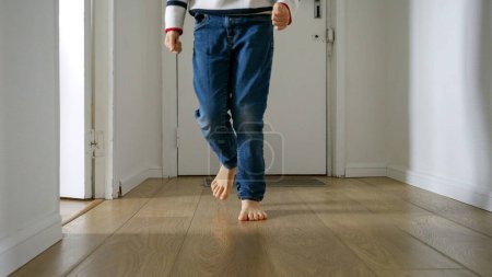 Photo for Little boy as running on a wooden floor in a long corridor at home. Happy childhood and the importance of playing at home for child development - Royalty Free Image