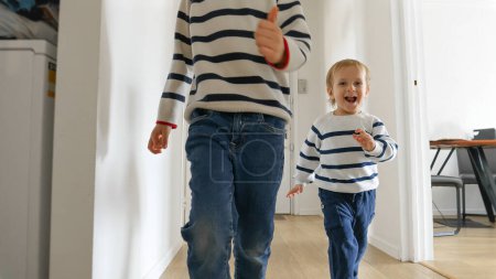 Foto de Dos niños pequeños son vistos corriendo por un largo corredor de madera en cámara lenta, sus caras felices que reflejan las alegrías del tiempo de juego de la infancia. Importancia del juego y la vinculación con los miembros de la familia - Imagen libre de derechos
