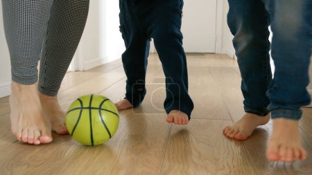 Photo for Happy family's feet as they kick a football back and forth on a wooden floor in a house corridor. The slow motion footage conveys the playful energy and excitement of childhood - Royalty Free Image