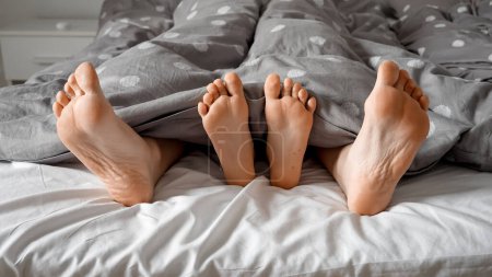 Foto de Primer plano de los pies de los padres y del niño sobresaliendo de debajo de la manta en la cama. Concepto de amor familiar, comodidad, infancia feliz y vida familiar - Imagen libre de derechos
