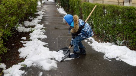 Téléchargez les photos : Petit garçon nettoyant la cour arrière ou la passerelle de la neige avec une pelle après une tempête de neige ou un blizzard - en image libre de droit