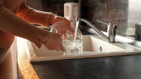 Téléchargez les photos : Gros plan de mains féminines laver bol en verre dans l'évier de la cuisine. Travail de femme au foyer, tâches ménagères, tâches ménagères - en image libre de droit