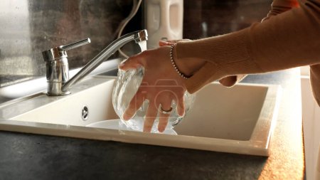 Téléchargez les photos : Gros plan de mains féminines avec anneaux et bracelet laver la vaisselle sale dans l'évier sur la cuisine. - en image libre de droit