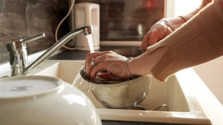 Photo for Closeup of elegant woman washing dishes in sink at home against sunset light. - Royalty Free Image