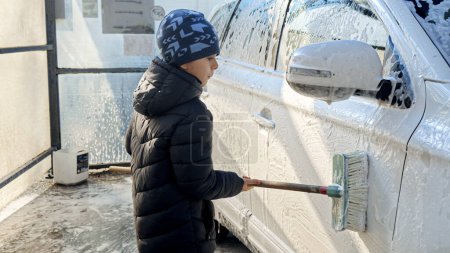 Photo for Little boy washing dirty car with soft brish on self service car wash. - Royalty Free Image