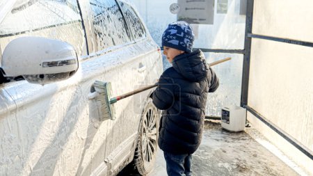 Foto de Niño pequeño lavando el coche en auto-servicio de lavado de autos. Concepto de crianza de los hijos, ayuda a los padres y cuidado del automóvil - Imagen libre de derechos