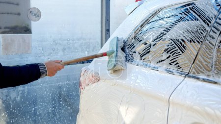 Foto de Primer plano del hombre limpiando su coche sucio con espuma de jabón y cepillo. Cuidado del automóvil, limpieza del transporte, coche sucio - Imagen libre de derechos
