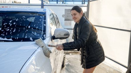 Foto de Hermosa mujer sonriente cuidando de su coche y lavando el automóvil por sí misma en el auto servicio de lavado de coches. - Imagen libre de derechos
