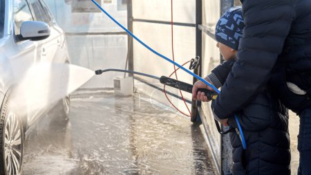 Téléchargez les photos : Petit fils avec père utilisant un jet d'eau pour laver et nettoyer la voiture au lavage de voiture en libre-service extérieur. - en image libre de droit