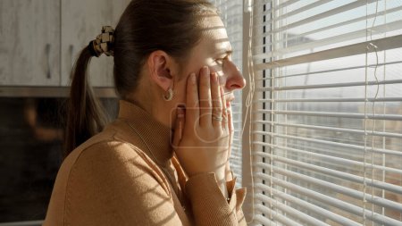 Foto de Mujer asustada y estresada siendo testigo de crimen o catástrofe mirando por la ventana a través de persianas. - Imagen libre de derechos