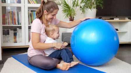 Photo for Young mother with her little baby son playing with fitball while doing fitness on mat at living room. Concept of healthcare, sports, childcare and kids development. - Royalty Free Image