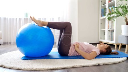 Photo for Young sporty woman doing fitness exercsises with inflatable fitness ball at home. - Royalty Free Image