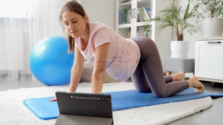 Foto de Mujer sonriente estirándose en la esterilla de fitness antes de la lección de video entrenamiento en línea. Concepto de salud, deportes y yoga en casa - Imagen libre de derechos