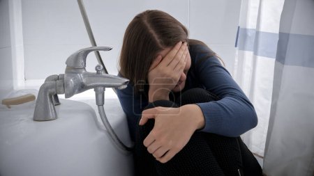 Téléchargez les photos : Femme bouleversée en pleurs assise dans un bain après avoir été victime d'abus ou de violence. - en image libre de droit