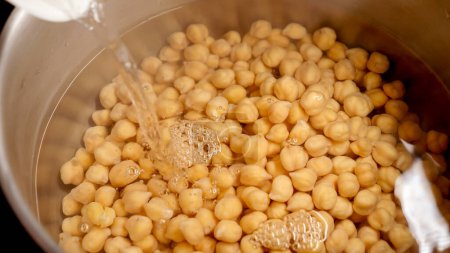Photo for Slow motion of pouring boiling water in pan with cooking chickpeas. Cooking egume, healthy nutrition, vegan food - Royalty Free Image