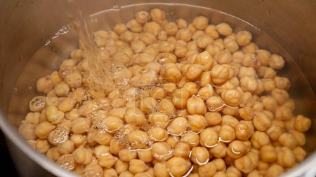Photo for Closeup of pouring hot water in pot with chickpeas. Cooking legume, healthy nutrition, vegan food - Royalty Free Image