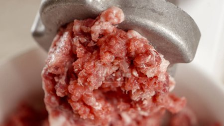 Téléchargez les photos : Macro shot de viande de bœuf hachée produite dans un hachoir électrique. Cuisiner à la maison, appareil de cuisine, alimentation saine, ingrédients pour hamburgers - en image libre de droit
