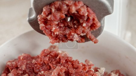 Photo for Closeup of red minced beef meat coming out of electric grinder and falling on plate. Cooking at home, kitchen appliance, healthy nutrition, hamburger ingredients - Royalty Free Image