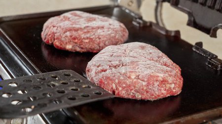 Téléchargez les photos : Gros plan de la main mettre des galettes de boeuf hamburger congelé sur le gril chaud. Cuisiner à la maison, appareil de cuisine, alimentation saine, ingrédients pour hamburgers - en image libre de droit