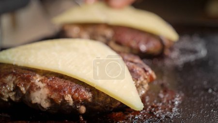 Photo for Closeup of putting cheese slices on cooking beef burger patties. Cooking at home, kitchen appliance, healthy nutrition, cheeseburger ingredients - Royalty Free Image