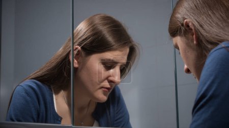 Foto de Molesto mujer estresada suspira en el baño y se ve en su reflejo en el espejo. Concepto de depresión, estrés, enfermedad mental y problemas, soledad y frustración - Imagen libre de derechos