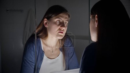 Téléchargez les photos : Femme bouleversée et fatiguée regardant son reflet dans un miroir. Concept de dépression, suicide, stress, maladie mentale, solitude et frustration - en image libre de droit