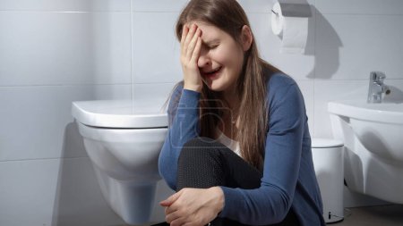 Téléchargez les photos : Jeune femme en pleurs assise par terre dans les toilettes. Concept de dépression, violence familiale, suicide, stress, solitude et frustration - en image libre de droit