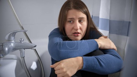Photo for Afraid woman sitting in bathroom and covering behind curtain. Concept of domestic violence victim, stress, danger at home, fear. - Royalty Free Image