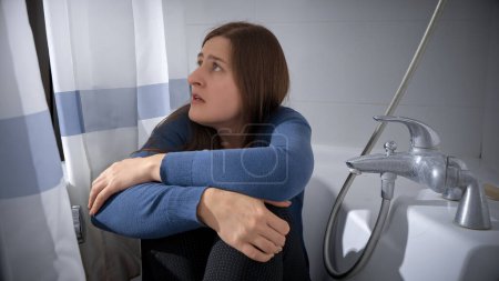 Foto de Mujer joven estresada que se esconde de una violencia criminal o doméstica en el baño. Mujer víctima de violencia doméstica causada por el marido - Imagen libre de derechos