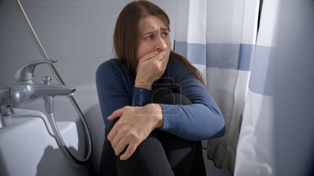 Foto de Mujer joven que se siente asustada escondiéndose en el baño y cerrando la boca para dejar de gritar. Concepto de víctima de violencia doméstica, estrés, peligro en el hogar, miedo y desastre - Imagen libre de derechos