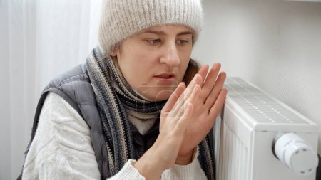 Foto de Retrato de una joven congelada en su apartamento tratando de calentarse en el radiador. - Imagen libre de derechos