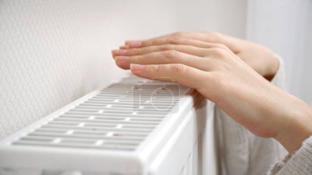 Foto de Primer plano de las manos femeninas calentándose sobre el radiador de pared en casa. - Imagen libre de derechos