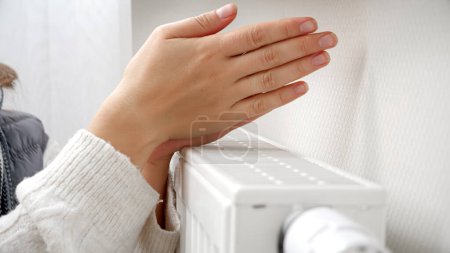 Foto de Primer plano de la mujer calentando sus manos en el radiador de calefacción en la casa. Concepto de crisis energética, facturas altas, sistema de calefacción roto, economía y ahorro de dinero en pagos mensuales de servicios públicos - Imagen libre de derechos