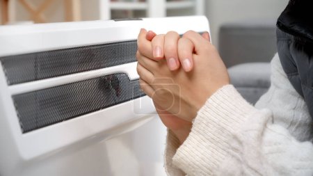 Foto de Primer plano de las manos femeninas frías que se calientan en el calentador eléctrico en casa. - Imagen libre de derechos