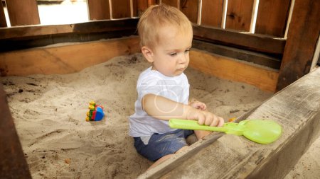 Foto de Niño jugando en arenero con juguetes de plástico y cavando arena. - Imagen libre de derechos