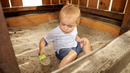 Téléchargez les photos : Joli petit garçon creusant du sable avec une pelle à jouets dans un bac à sable au parc. Enfants jouant à l'extérieur, enfants s'amusant, vacances d'été et vacances - en image libre de droit