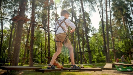 Foto de Niño pequeño cruzando el puente de madera en el parque de aventura de cuerda en el bosque. Infancia activa, estilo de vida saludable, niños jugando al aire libre, niños en la naturaleza - Imagen libre de derechos