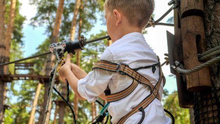 Photo for Closeup of little boy clamping safety rope with hook before riding on zip line. Active childhood, healthy lifestyle, kids playing outdoors, children in nature - Royalty Free Image