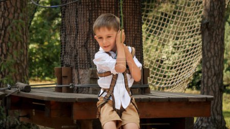Photo for Handheld shot of smiling boy playing in adventure park and riding on the zip line. Active childhood, healthy lifestyle, kids playing outdoors, children in nature - Royalty Free Image