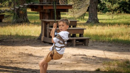 Téléchargez les photos : Petit garçon chevauchant sur la tyrolienne au camp d'été en forêt. Enfance active, mode de vie sain, enfants jouant à l'extérieur, enfants dans la nature - en image libre de droit