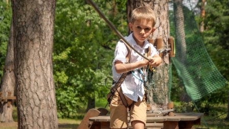Photo for Portrait of little boy walking over strung rope between trees in outdoor adventure park. Active childhood, healthy lifestyle, kids playing outdoors, children in nature - Royalty Free Image