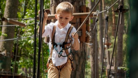 Téléchargez les photos : Portrait d'un petit garçon franchissant des obstacles au parc d'entraînement d'escalade en plein air. Enfance active, mode de vie sain, enfants jouant à l'extérieur, enfants dans la nature - en image libre de droit